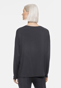 Długo rękawowa, ciemnoszara koszula wykonana z miękkiego materiału w luźnym kroju, z szerokim dekoltem i delikatnymi rozcięciami po bokach dla większego komfortu.