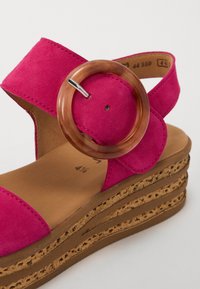 Fuchsia suède sandaal met een brede band, een ronde bruine accent en een kurken plateauzool met uitsnijdingen.