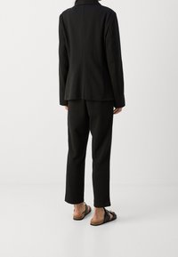 Czarna, dopasowana marynarka i pasujące spodnie z miękkiego materiału o luźnym kroju. Outfit dopełniają sandały na korkowej podeszwie.