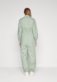 Mono verde claro con cintura y puños elásticos, mangas largas y dos bolsillos traseros. Tejido suave con un diseño minimalista.