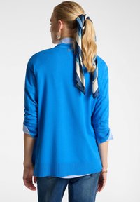 Maglione blu con maniche lunghe, texture morbida, orlo a coste, indossato sopra una camisa a righe bianca e blu, accentuato da una sciarpa di seta.