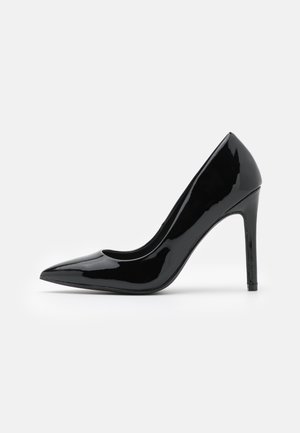 Chaussure à talon haut en cuir verni noir, à bout pointu et talon aiguille, vue de profil sur fond blanc.