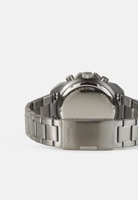 Fossil Edelstahl-Uhr mit einem silbernen Armband. Merkmale sind eine glatte Lünette, eine strukturierte Krone und ein minimalistischer, polierter Rücken.