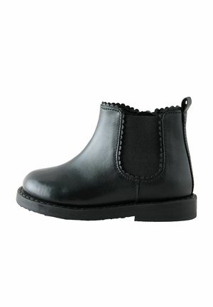 Schwarzer knöchelhoher Lederstiefel mit gezacktem Besatz, elastischem Seitenpanel und Zuglasche auf flacher Sohle, seitlich dargestellt.