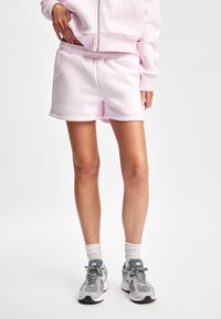 Lys rosa bomullsshorts med elastisk midje, jevn tekstur og avslappet passform, parret med grå joggesko og hvite sokker.