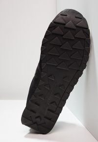 Suola di scarpa sportiva nera con superficie testurizzata e modelli di impuntura triangolari per la presa, realizzata in gomma con dettagli del logo.