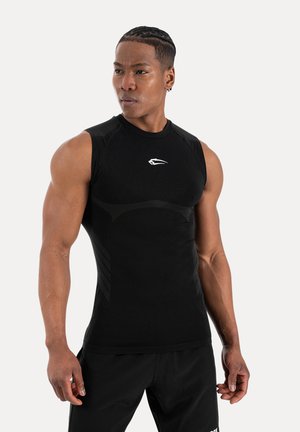 Homme musclé aux cheveux tressés portant un débardeur de sport noir ajusté et un short noir, regardant sur le côté.