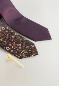 Duosi kaklaraiščiai: vienas vientisas tamsiai violetinis su tekstūruotu raštu, o kitas su gėlių raštu tamsiai žalias, burbulių ir grietinėlės spalvos. Įeina auksinis kaklaraiščio segtukas.