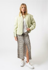 Ljusgrön vadderad jacka med rundad krage, vit strukturerad topp och en beige kjol med leopardmönster och sidoklyvning, i kombination med vita sneakers.