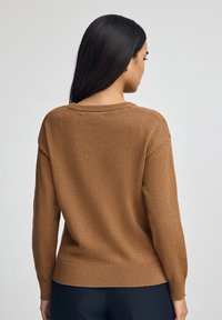 Brązowy dzianinowy sweter z okrągłym dekoltem, prążkowanym dołem i mankietami oraz luźnym krojem. Materiał jest miękki w dotyku i ma minimalną ilość szwów.