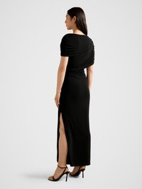 Black, form-fitting evening dress with ruched short sleeves, draped back, and a thigh-high side slit; smooth, slightly textured fabric.