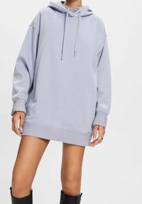 Sudadera de gran tamaño en un suave tono morado claro, con capucha ajustable y puños y dobladillo acanalados. Presenta sutiles acentos de rayas en las mangas. Textura de tela suave.