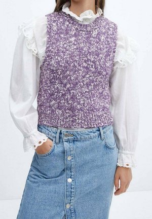 Personne portant un gilet sans manches violet tricoté sur une blouse blanche avec des poignets et un col à volants, associé à une jupe en jean à boutons.