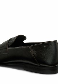 Svart läder loafer med texturerad yta, böjd krage och diskret logodetalj på hälen. Platt gummisula, minimalistisk design.