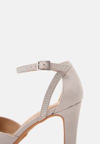 Chaussure à talon haut gris clair avec bout ouvert, en daim, bride de cheville ornée de strass et talon profilé.