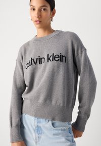 Hallist kootud sviiter, millel on vabalt langev lõige, ribaga varrukas ja äär, ning esiküljel on kontrastse musta värviga "calvin klein" logo.