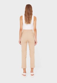 Beige high-waisted pants with a slim fit and straight legs, made from a smooth fabric. Features a clean design with no visible hardware.