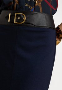 Melns ādas josta ar zelta sprādzi, valkāta virs tumši zilas svārku un rakstainas tumšas blūzes, papildināta ar bruņurupuča čaulas aproci un zelta pulksteni.