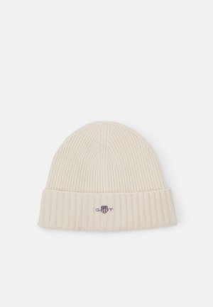 Ribbed cream knit beanie with a folded cuff, featuring a small embroidered logo on the front, made from soft fabric.