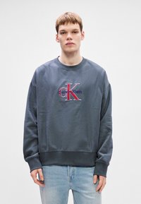 Sweatshirt azul-marinho com decote redondo, ajuste descontraído e logotipo bordado "Calvin Klein" em vermelho e branco. Fabricado em um suave tecido de mistura de algodão.