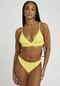 Ensemble de bikini jaune avec un motif floral texturé, comprenant un haut triangulaire et un bas taille basse, tous deux dotés de fines bretelles ajustables.