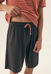 Szare szorty sportowe z elastycznym pasem i koralowym sznurkiem; noszone z pasiastą koszulką w kolorze rdzy, o gładkiej, lekkiej teksturze.