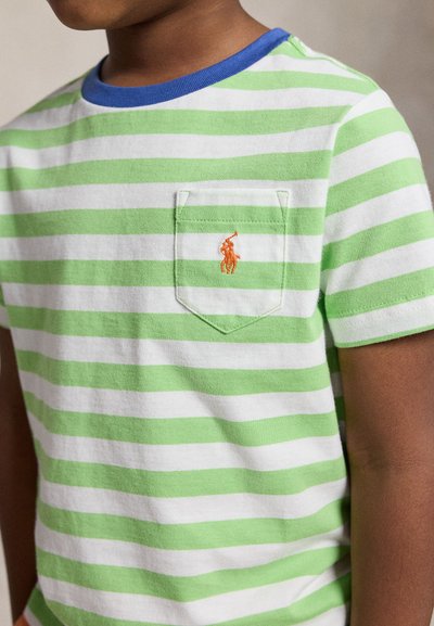 Niño con camiseta de rayas horizontales verdes y blancas, con cuello azul y un pequeño logo naranja bordado en el bolsillo del pecho.