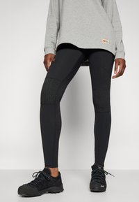 Svarta träningsleggings med texturerade knäpaneler och en åtsittande design, tillsammans med en grå långärmad topp och svarta utomhusskor.