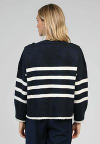 Pull en laine bleu marine avec des rayures horizontales blanches, présentant une coupe décontractée, des poignets larges et un ourlet doux et duveteux. Vue arrière montrée.