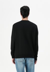 Schwarzer Pullover mit Rundhalsausschnitt, langen Ärmeln und gerippten Bündchen. Getragen über hellblauen Jeans mit einer einfachen, glatten Textur.