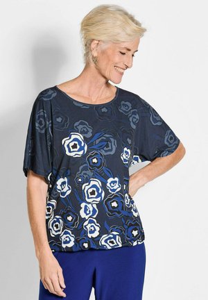 Schwarzes und blaues Oberteil mit floralem Muster, kurzen Ärmeln, rundem Halsausschnitt und lockerer Passform. Es hat große weiße und marineblaue Blumen auf einem dunklen Hintergrund.