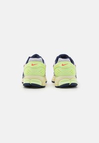 Sapatilhas de corrida Nike em azul marinho e amarelo néon. Parte superior em malha com calcanhar texturizado, detalhes em vermelho e sola acolchoada. A vista traseira mostra um design bicolor.