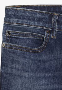 Jeans de mezclilla de un azul oscuro con una textura suave, que presentan costuras en contraste, un pequeño bolsillo frontal y una cintura clásica.