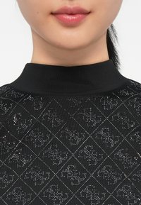 Top nero con colletto alto, caratterizzato da una trama a motivi a forma di diamante con accenti lucidi. Tessuto liscio con una leggera lucentezza.