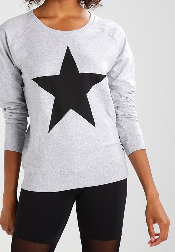 Sudadera gris con un gran gráfico de estrella negra en la parte delantera; tiene mangas largas y un escote redondeado, combinada con leggings negros.