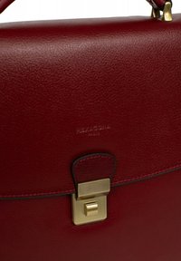 Bordeaux leren tas met gouden accenten. Heeft een rechthoekige vorm, een klap sluiting en reliëf logo detail. Glad textuur.