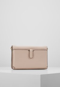 Beige nahkalompakko, jossa on teksturoitu pinta, suorakulmainen muoto, etukansi, joka on kiinnitetty hihnalla, ja hillitty kultainen yksityiskohta.