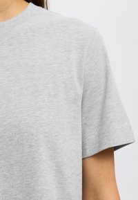 Camiseta de algodón gris con cuello redondo y mangas cortas, con una textura suave y detalles de costura mínimos.
