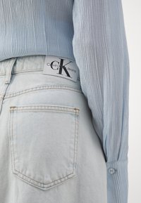 Lyseblå ribstrikket skjorte med lange ærmer, kombineret med lyseblå vaskede denimjeans med en synlig baglomme og et Calvin Klein-mærke.