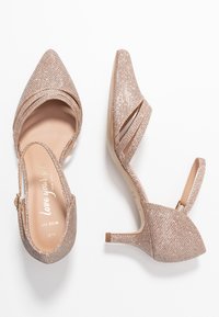 Chaussures à talons aiguilles en rose doré clair avec des pointes effilées, une finition texturée scintillante, et un talon effilé, dotées d'une sangle ajustable au niveau de la cheville.