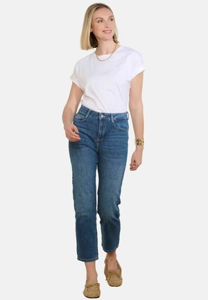 High-waisted blue jeans with a straight cut, made of denim, paired with a white short-sleeve t-shirt and beige moccasin-style shoes.