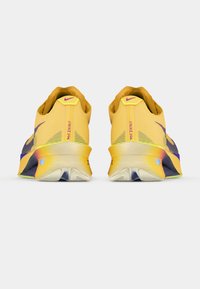 Nike tenisice za trčanje s gornjim dijelom u žutoj boji, teksturiranom tkaninom i ljubičastim akcentima. Imaju amortizirani đon s prepoznatljivim oblikom.