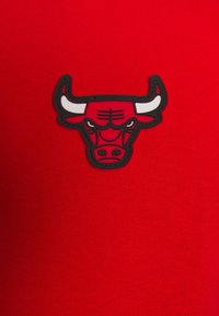 Červená tkanina má uprostřed vyvýšené logo Chicago Bulls s černým obrysem, které zobrazuje hlavu býka s výraznými rohy a detaily obličeje.