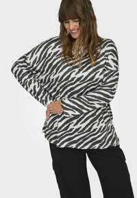 Top a maniche lunghe, di taglio ampio, con righe zebrate bianche e nere su tessuto morbido. Collo rotondo, spacchi laterali e design rilassato.