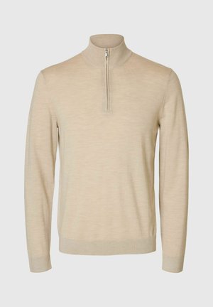 Bežinis vilnonis megztinis su aukštu apykakle ir ketvirčio užtrauktuku. Yra ilgos rankovės ir lygi, šiek tiek tekstūruota apdaila.