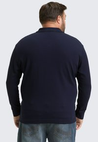 Marineblauwe polo met lange mouwen, voorzien van een geribbeld structuur en een klassieke kraag, gecombineerd met denim jeans met gedetailleerde stiksels.