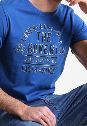 Blue cotton T-shirt featuring graphic print in white and black text. Crew neck, short sleeves, with "THE BOWERY" prominently displayed.