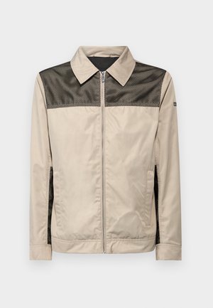 Chaqueta beige con un panel de malla negra en los hombros. Cuenta con un cuello, cierre frontal y bolsillos laterales. Textura suave.