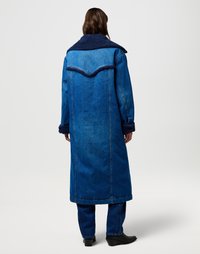 Lang denim jas met een marineblauwe fleece kraag, met een blauwe gradient en gestructureerde stof. Vergezeld van bijpassende blauwe broeken en zwarte laarzen.