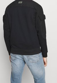 Svart sweatshirt med en slät textur, ribbade muddar och en etikett på baksidan. Matchas med ljusblå jeans med en urtvättad finish.